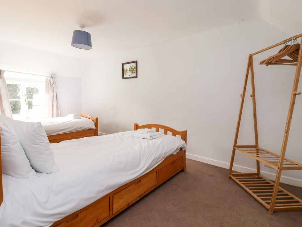 A bedroom with two single beds white sheets wooden frames a wooden clothes rack and a window with curtains at Cliff Cottage in Thirsk