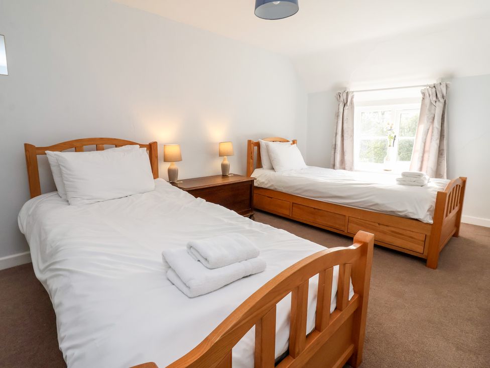 A bedroom with two wooden single beds with white bedding and folded towels on each bed at Cliff Cottage in Thirsk