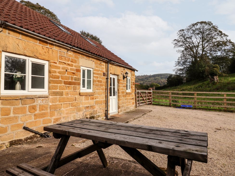 A stone cottage exterior with a wooden picnic table and a fenced yard at Cliff Cottage in Thirsk