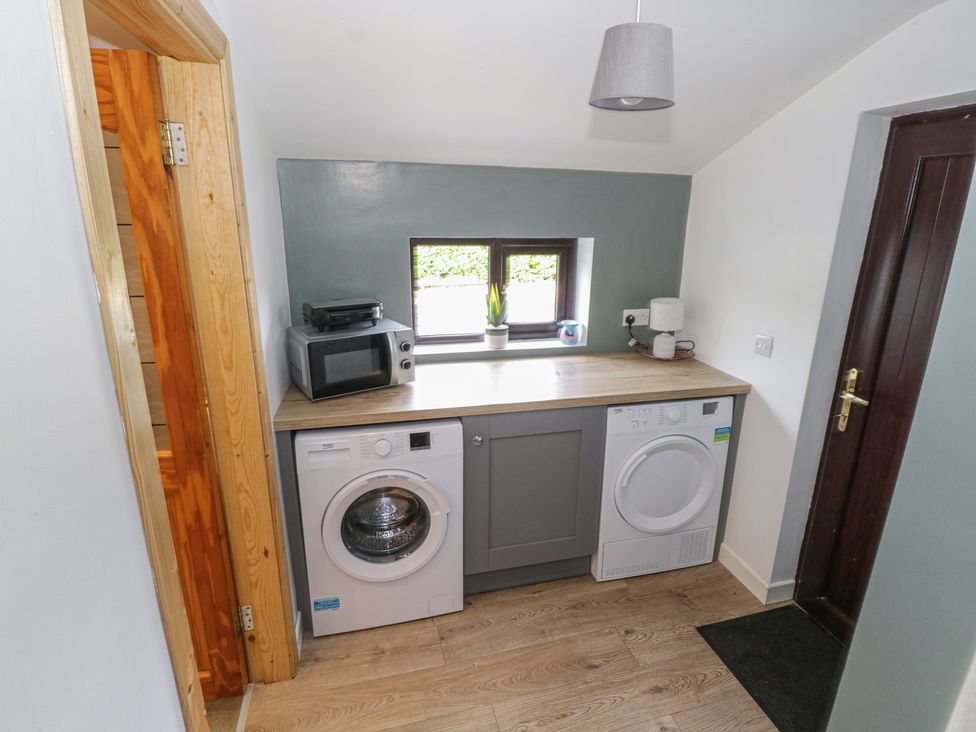 A laundry room with washing machine dryer countertop microwave and small window at Kates Cottage in Killawullaun near Ballintubber County Mayo
