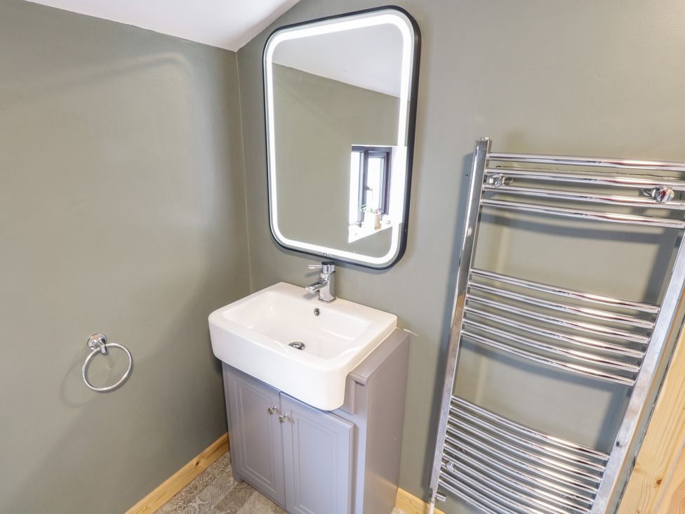 A bathroom sink with a lit mirror cabinet and a towel rail at Kates Cottage in Killawullaun near Ballintubber County Mayo