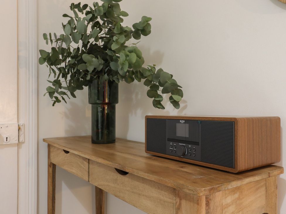 A wooden table with a green vase of leaves and a radio on top at Mabel in Whitstable
