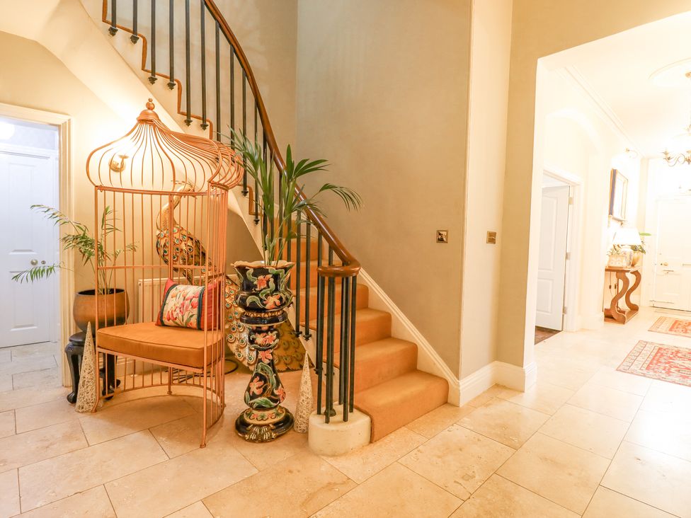 A hallway with a staircase and a birdcage chair with a cushion and decorative plants at 3 Old Market Place in Harleston