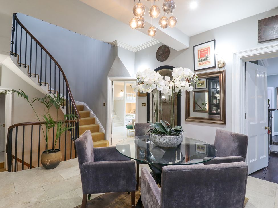 A dining area with a round glass table and four grey chairs near a staircase with a wooden handrail at 3 Old Market Place in Harleston