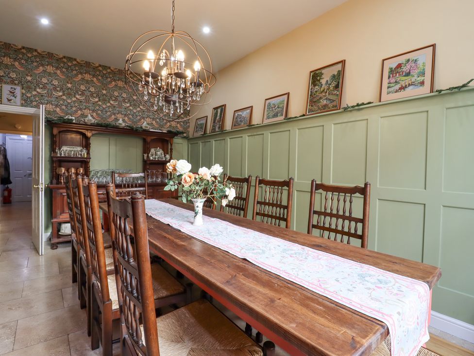 A dining room with a long wooden table and chairs a chandelier flowers in a vase and framed pictures on green paneled walls at 3 Old Market Place in Harleston