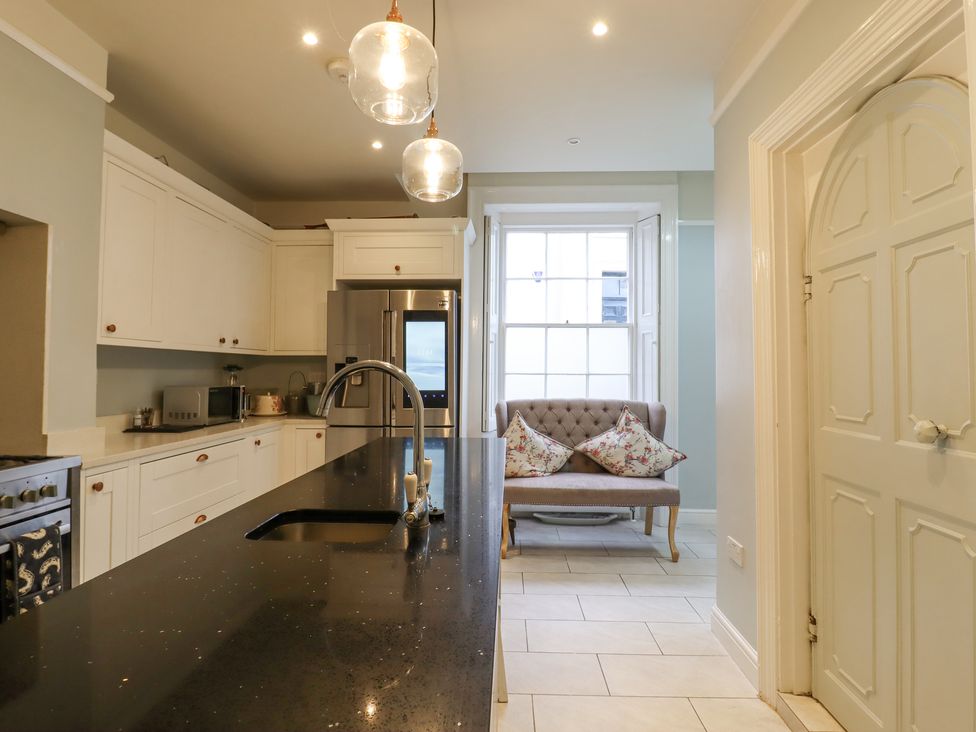 A kitchen with white cabinets a black countertop sink a stainless steel refrigerator and a tufted sofa with floral cushions at 3 Old Market Place in Harleston