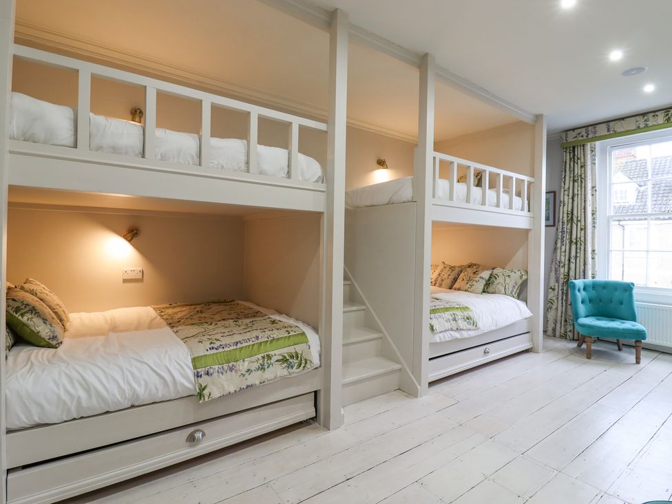 A bedroom with bunk beds a blue chair and a window at 3 Old Market Place in Harleston