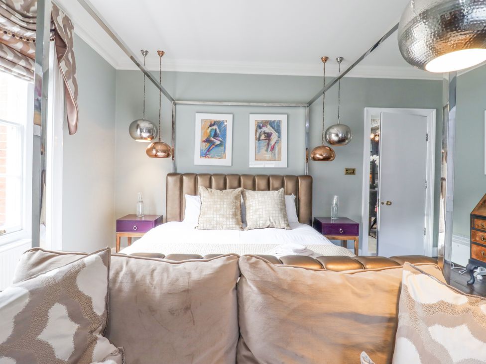 A bedroom with a four-poster bed two pillows two bedside tables with lamps and a sofa at 3 Old Market Place in Harleston