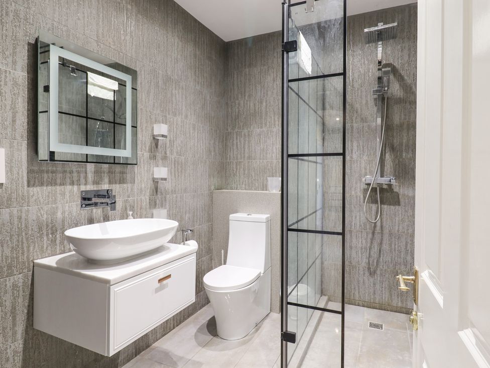 A bathroom with a washbasin, toilet, shower area, and mirror at 3 Old Market Place in Harleston