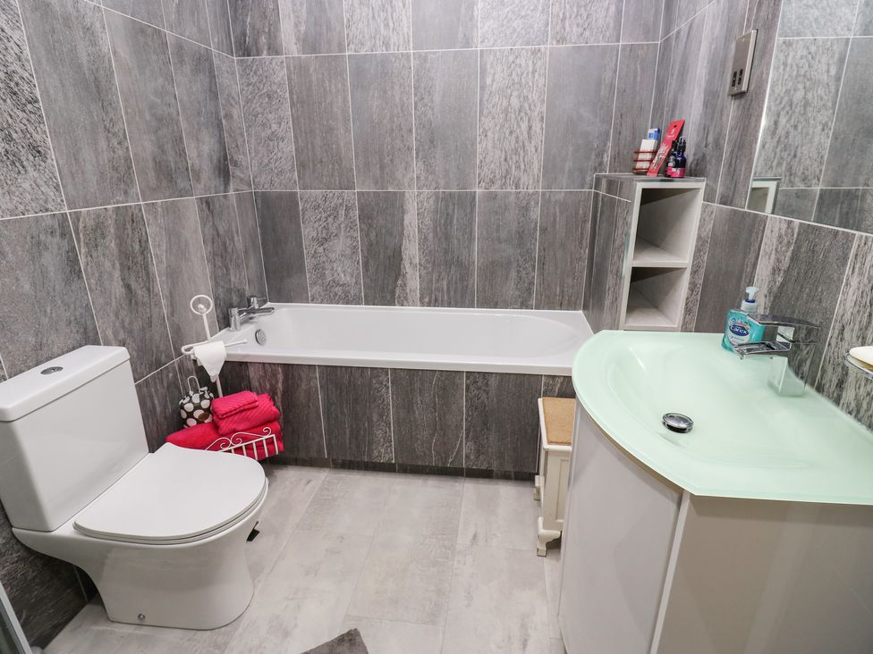 A bathroom with a bathtub a toilet a sink and shelves with toiletries at New Heights in Oxenhope
