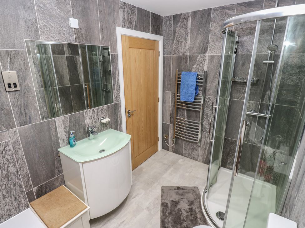 A bathroom with a curved glass shower enclosure a wooden door a sink with a mirror and a towel rack with a blue towel at New Heights in Oxenhope