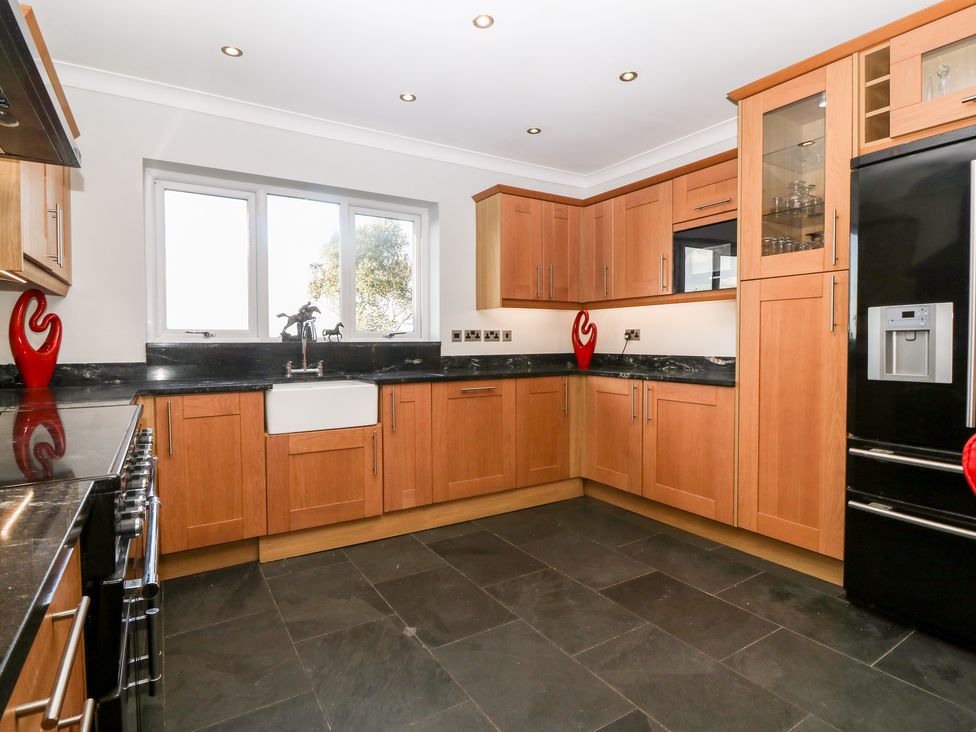 A kitchen with wooden cabinets black countertops a white farmhouse sink a black refrigerator and a stove at Tyn Rallt Ice Cream Farm Malltraeth near Newborough