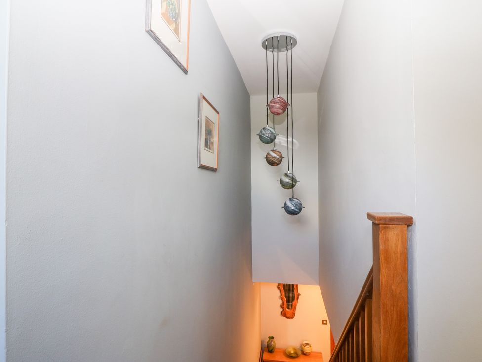 A staircase with wooden railing picture frames on a wall and a hanging light fixture with spherical shades at Tyn Rallt Ice Cream Farm in Malltraeth near Newborough