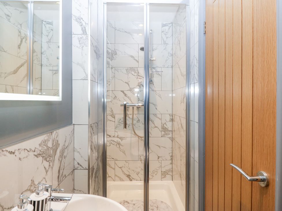 A bathroom with a shower enclosure, a sink, soap dispensers, a mirror, and a wooden door at Tyn Rallt Ice Cream Farm Malltraeth near Newborough
