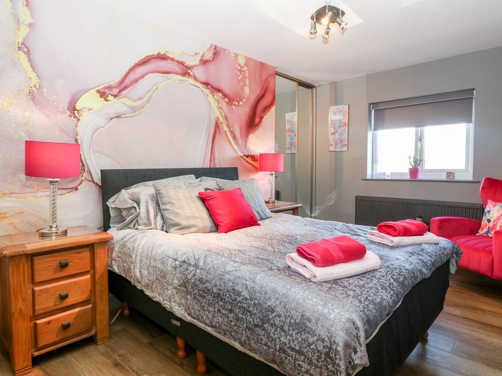 A bedroom with a bed with pillows and folded towels bedside tables with lamps a red chair a window and a closet with mirrored doors at Tyn Rallt Ice Cream Farm Malltraeth near Newborough
