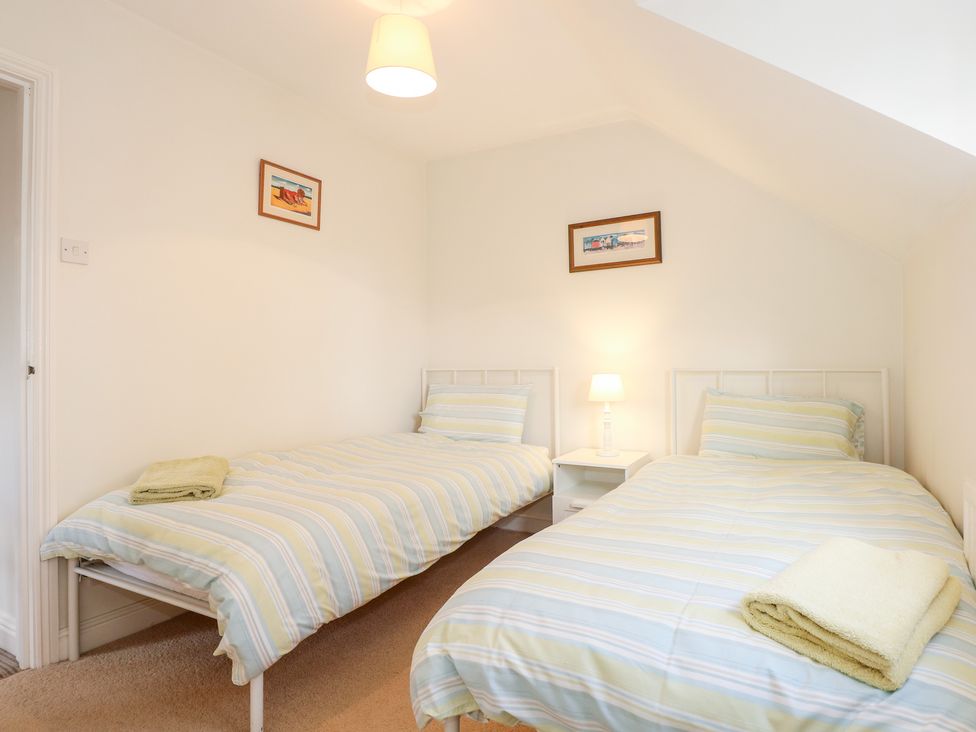 A bedroom with two single beds with striped bedding and a nightstand with a lamp at 1 Crowlands Cottages in Holt