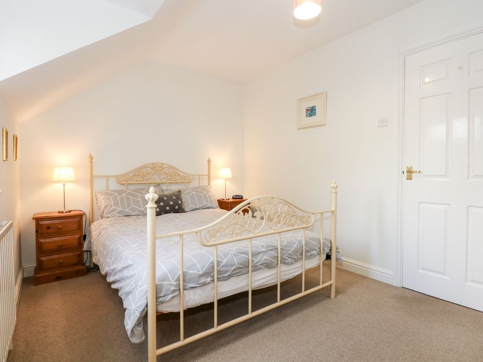 A bedroom with a metal bed frame two wooden bedside tables with lamps and a closed white door at 1 Crowlands Cottages in Holt