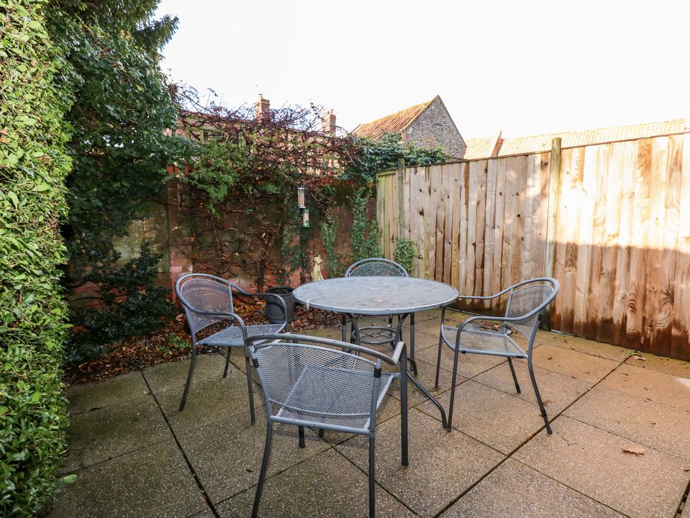An outdoor patio area with a metal round table and four metal chairs surrounded by a wooden fence and greenery at 1 Crowlands Cottages in Holt