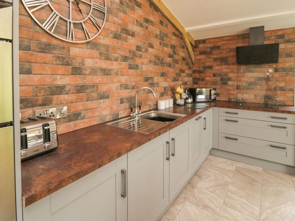 A kitchen with gray cabinets a brown countertop a stainless steel sink a toaster microwave and brick walls at Windy Willows in Okehampton