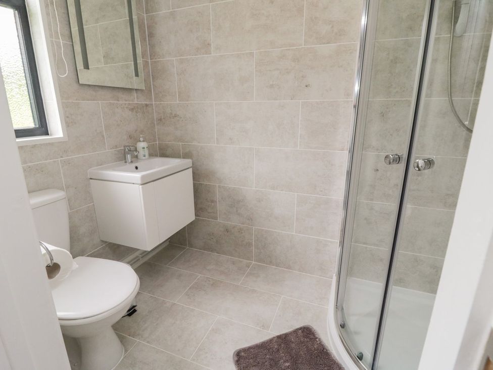 A bathroom with a toilet sink mirror and curved glass shower at Windy Willows in Okehampton