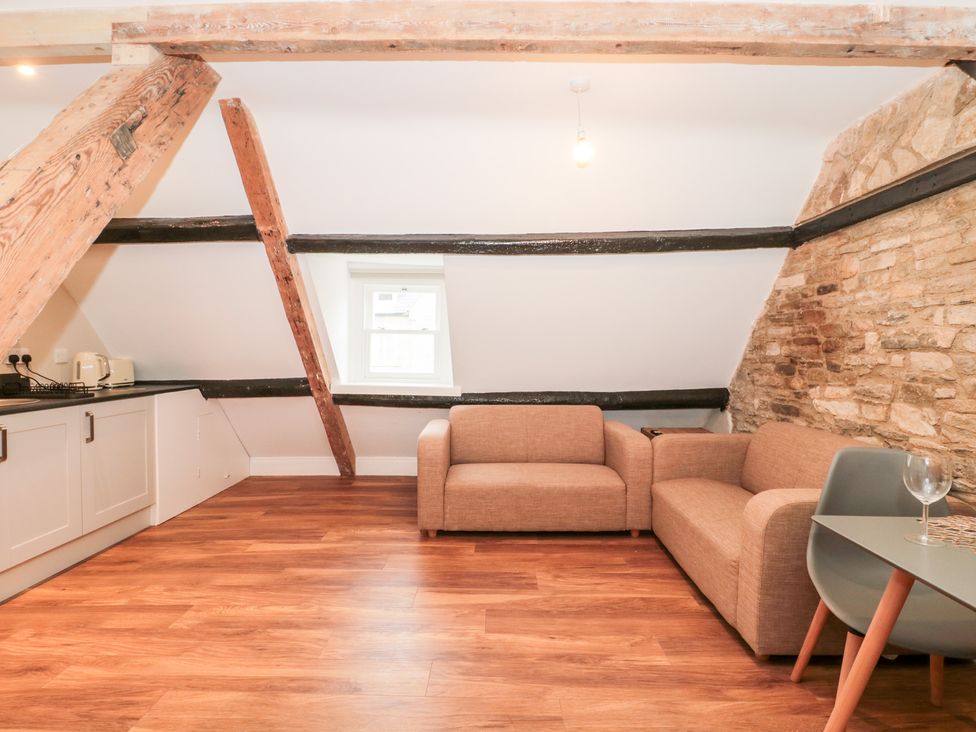 A room with wooden beams a small kitchen area a brown sofa and a table with chairs at Purbeck Hotel Apartments - Flat 5 in Swanage