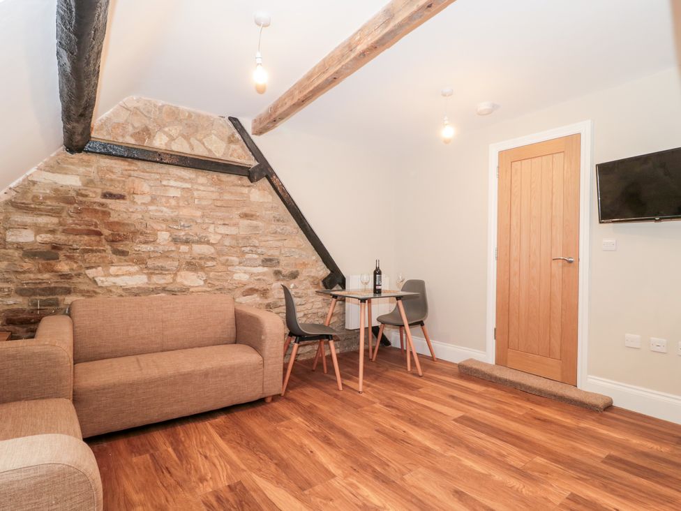 A room with a brown sofa a small table with two chairs a wooden door and a wall mounted television at Purbeck Hotel Apartments - Flat 5 in Swanage