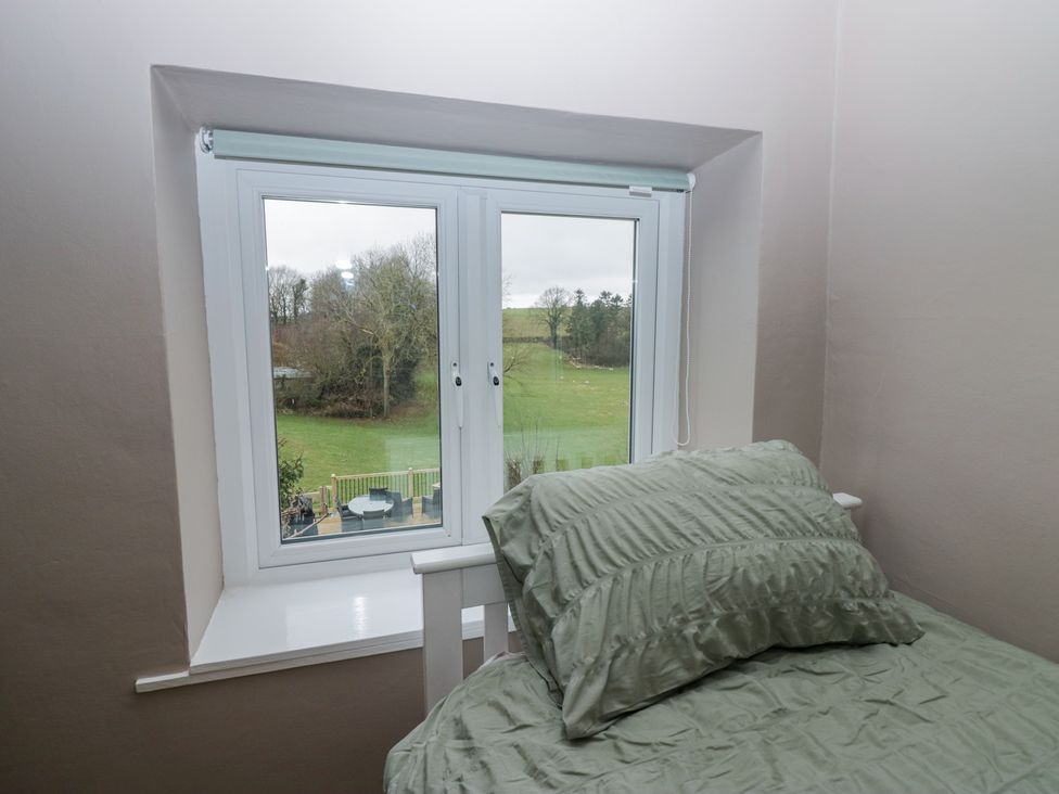 A bedroom with a bed near a window showing a view of a green field and trees at Willow Cottage in Silverdale