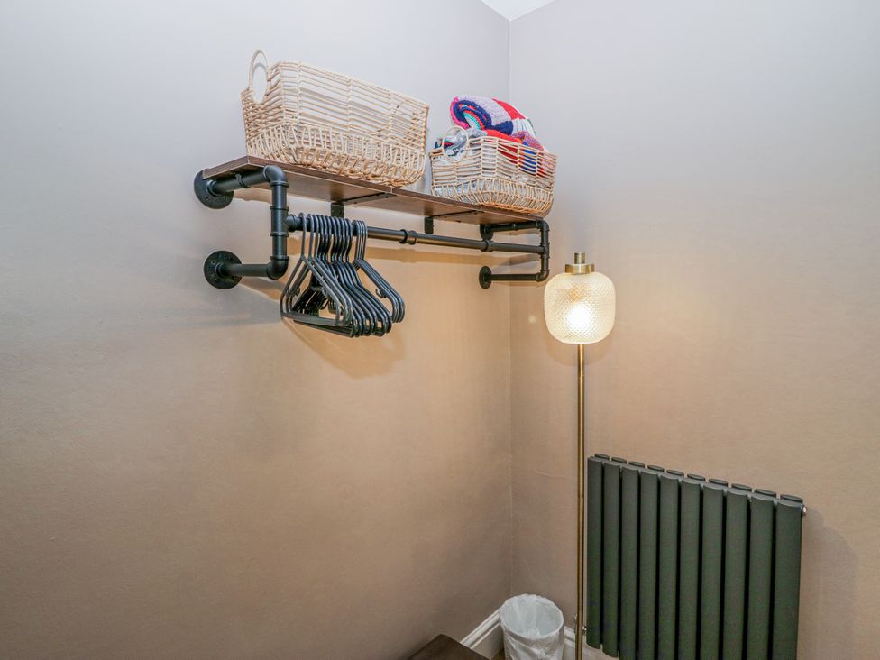 A corner with a wall-mounted shelf holding baskets, black hangers, a floor lamp and a radiator at Willow Cottage in Silverdale