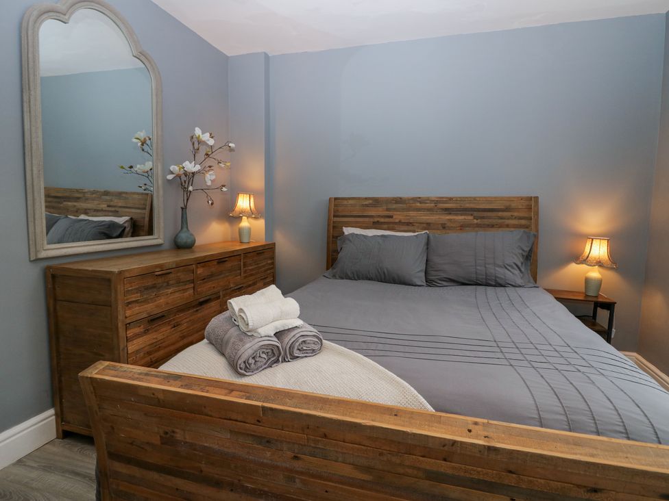 A bedroom with a wooden bed and dresser blue walls lamps and folded towels at Willow Cottage in Silverdale