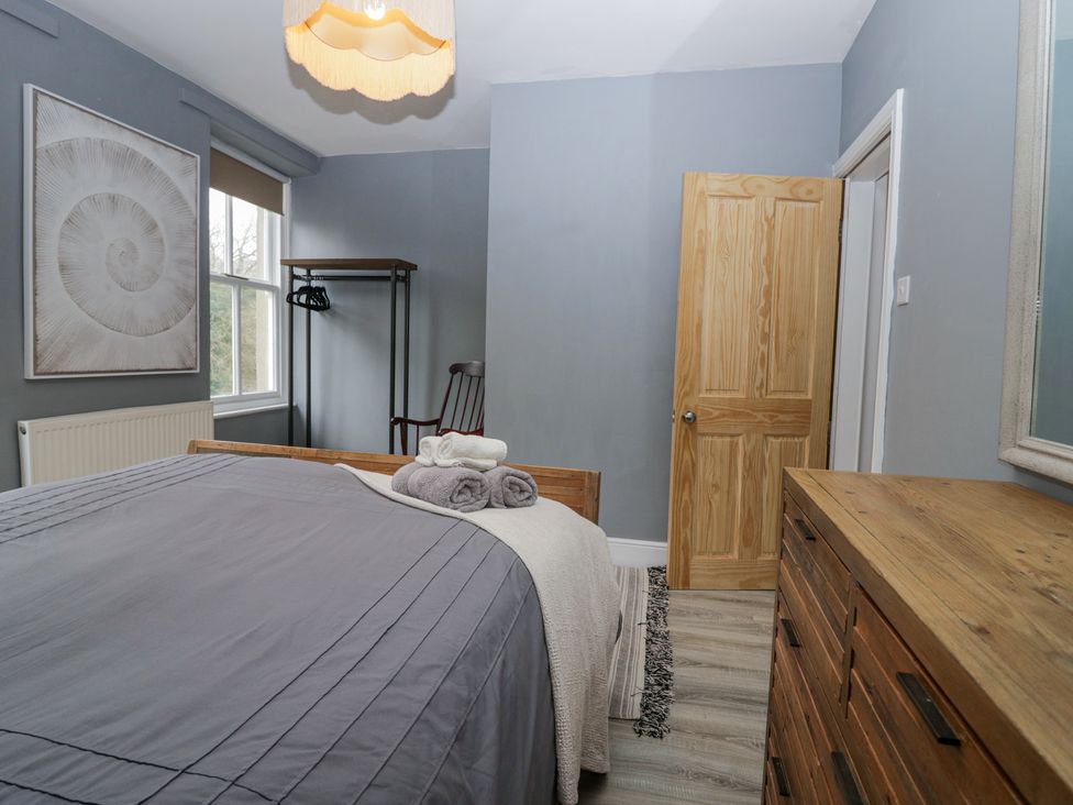 A bedroom with a wooden bed and dresser a window with a framed shell picture and an open wooden door at Willow Cottage in Silverdale