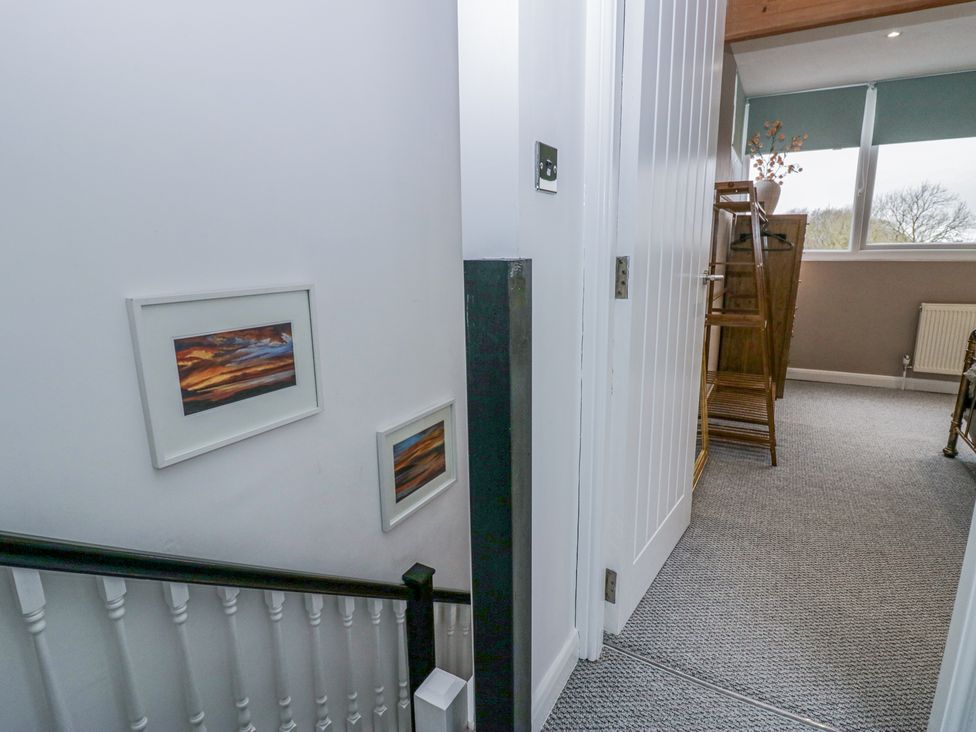 A hallway with stairs and framed pictures on the wall leading to a bedroom with a wooden wardrobe and window in Willow Cottage Silverdale
