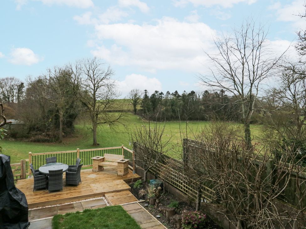 A wooden deck with outdoor furniture overlooking a green field with trees at Willow Cottage in Silverdale