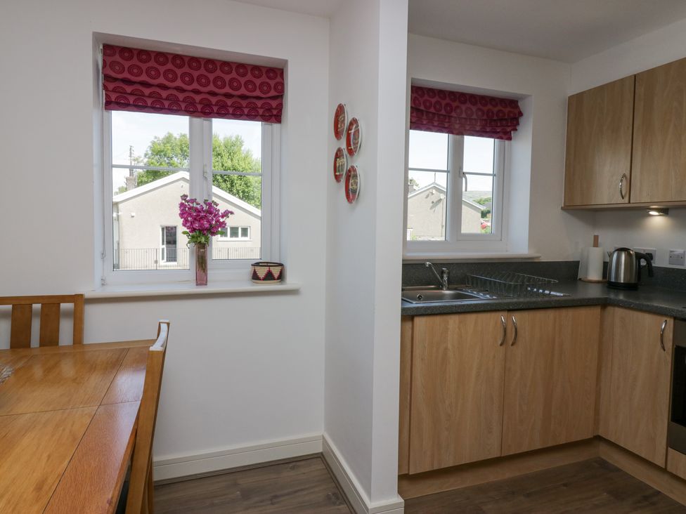 A kitchen and dining area with wooden cabinets wooden table and red patterned window blinds at Ingle View in Ingleton