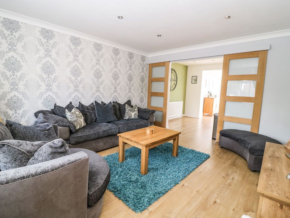 A living room with grey sofas a wooden coffee table blue rug and sliding doors at The Whyte Retreat in Hornsea