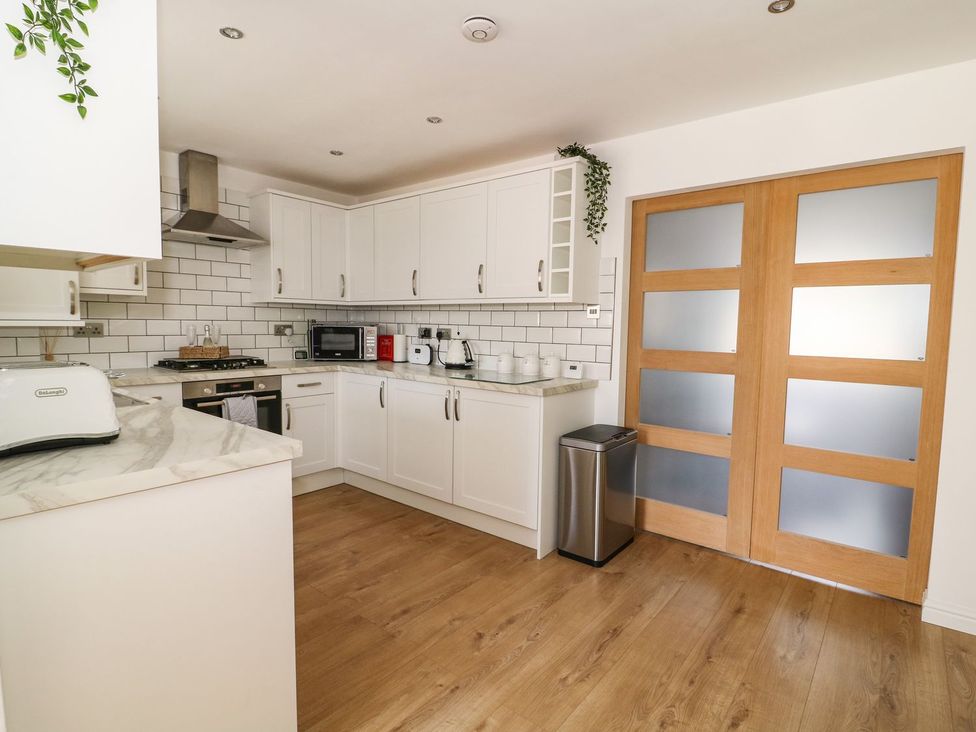 A kitchen with white cabinets appliances wooden floor and frosted glass wooden doors at The Whyte Retreat in Hornsea
