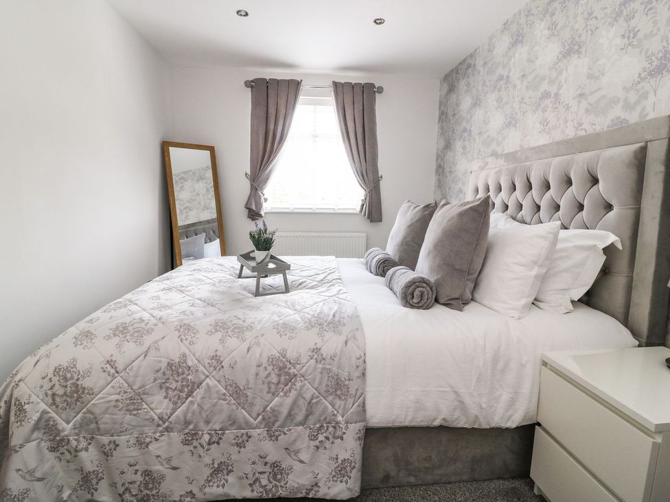 A bedroom with a bed featuring grey pillows and blanket a full length mirror next to the window and a white bedside table at The Whyte Retreat in Hornsea