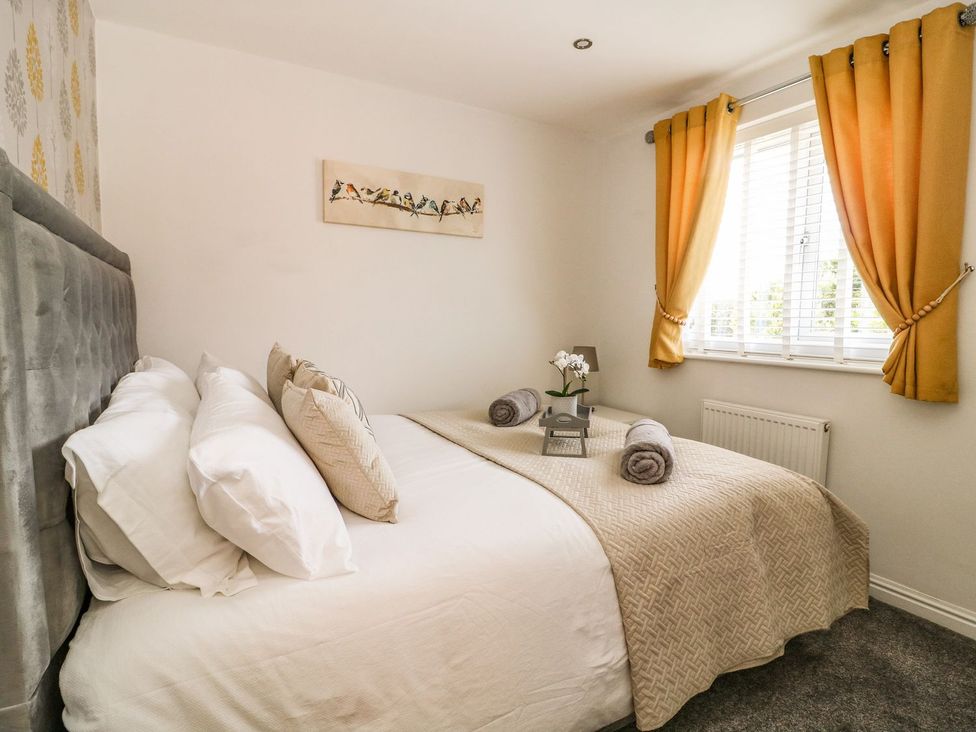 A bedroom with a bed with pillows and rolled towels near a window with orange curtains at The Whyte Retreat in Hornsea