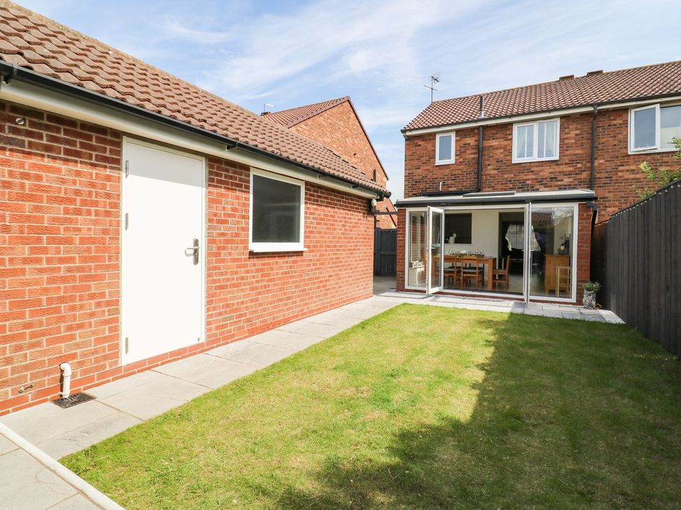 A backyard with a lawn and patio doors leading to a dining room at The Whyte Retreat in Hornsea