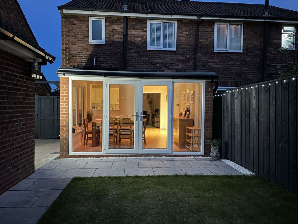 A backyard with a grass lawn and a paved patio leading to a house with large glass doors at The Whyte Retreat in Hornsea