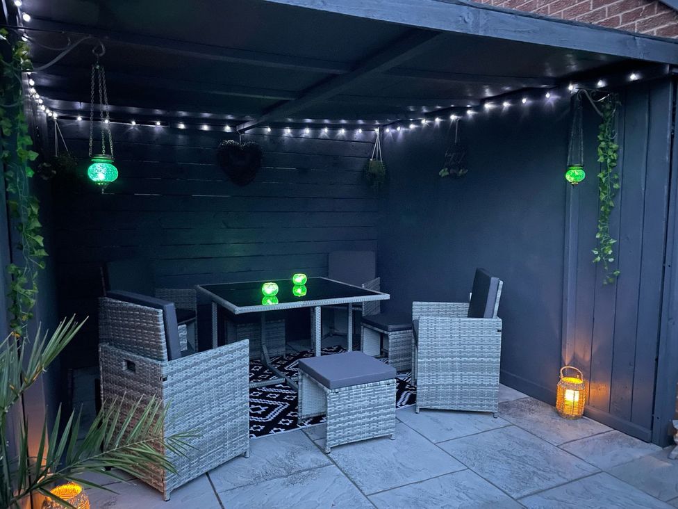 An outdoor seating area with a table and chairs under a covered patio with string lights and hanging plants at The Whyte Retreat in Hornsea