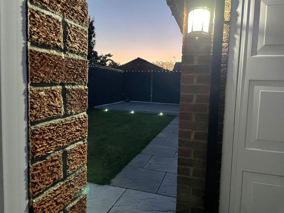 A backyard with a brick wall and patio lights near a door at The Whyte Retreat in Hornsea