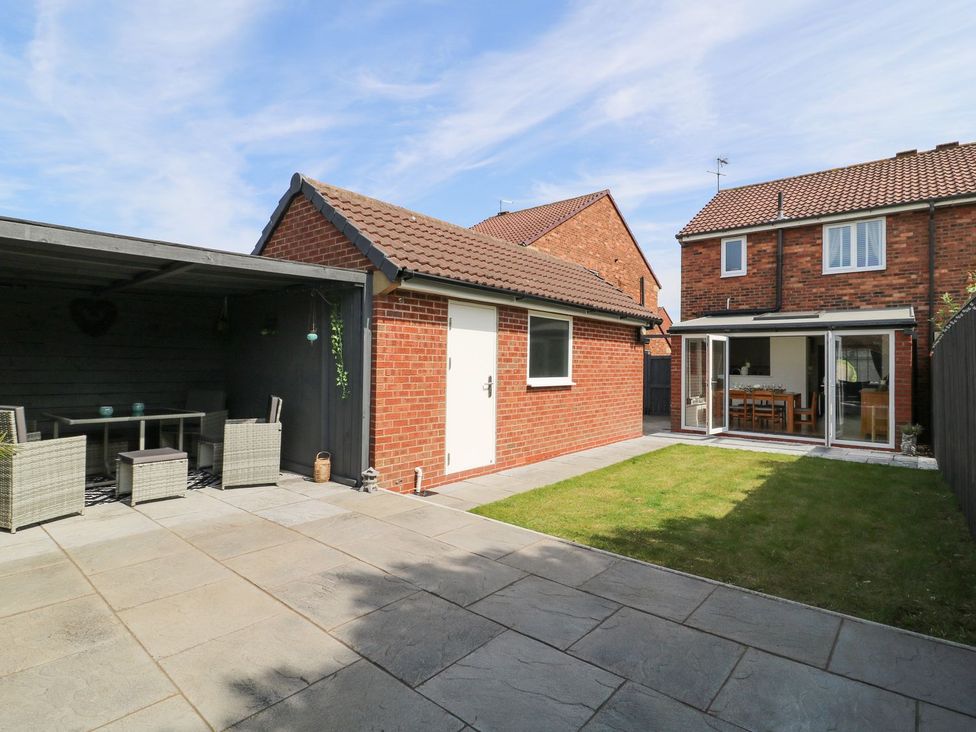 A backyard with patio furniture under a covered seating area and open doors to a dining room at The Whyte Retreat in Hornsea