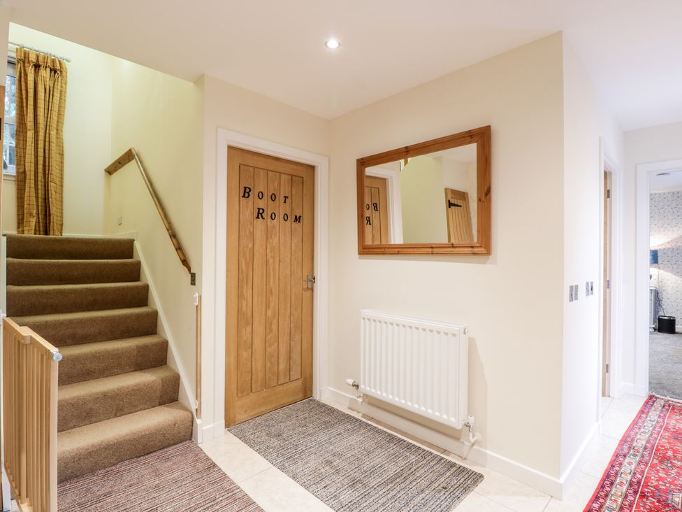 A hallway with carpeted stairs a wooden door labeled boot room a wall mirror and rugs at Oakbank in Carrutherstown near Annan