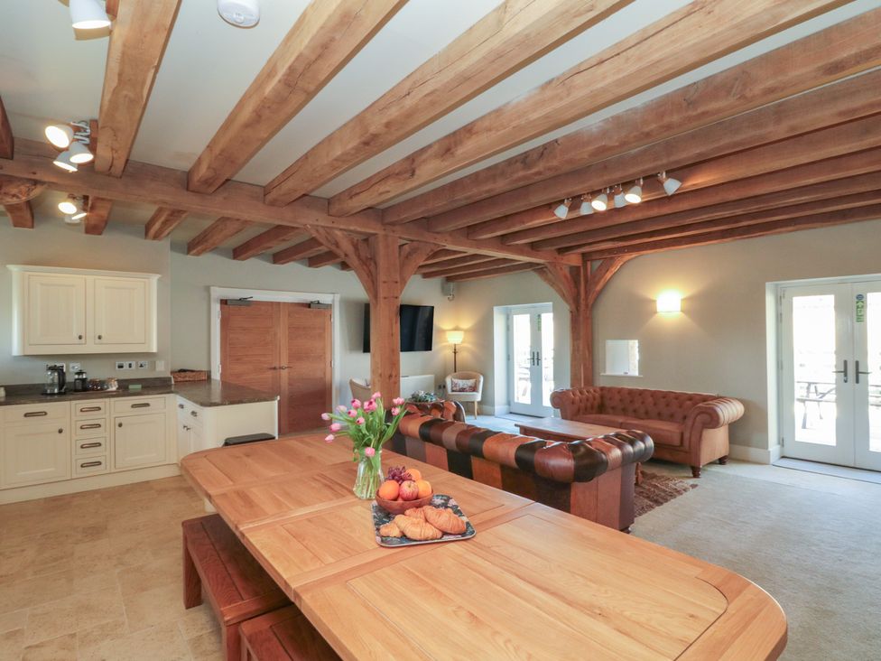 A living room with wooden beams ceiling a wooden table with flowers and croissants a leather sofa and armchair at The Barn Helperby near Boroughbridge