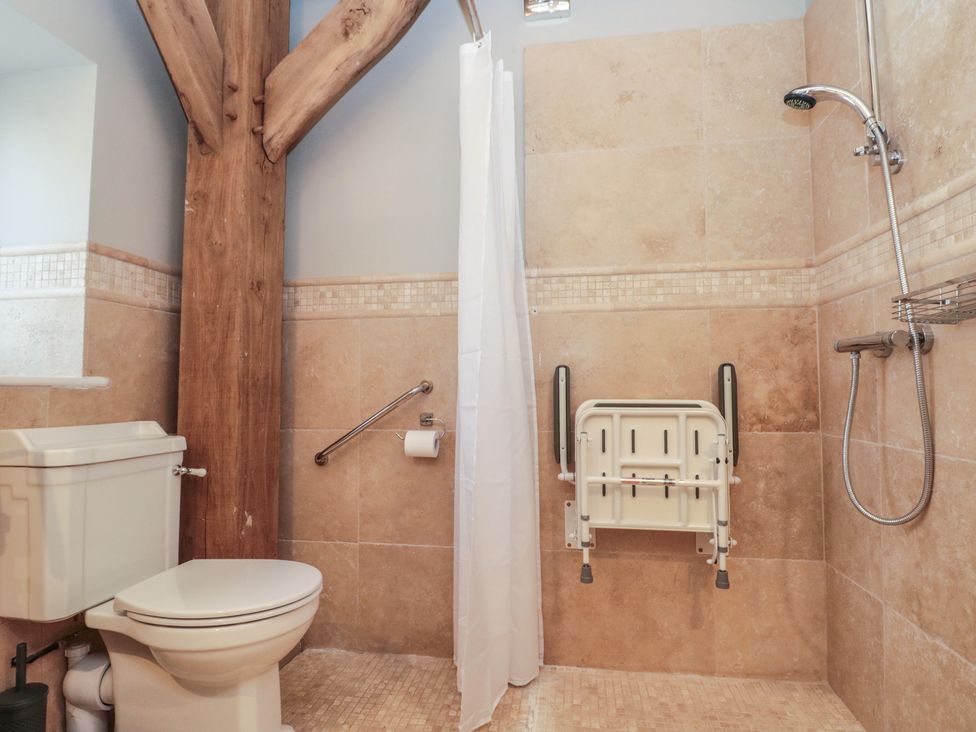 A bathroom with a toilet a shower area with a foldable seat and a wooden beam at The Barn Helperby near Boroughbridge