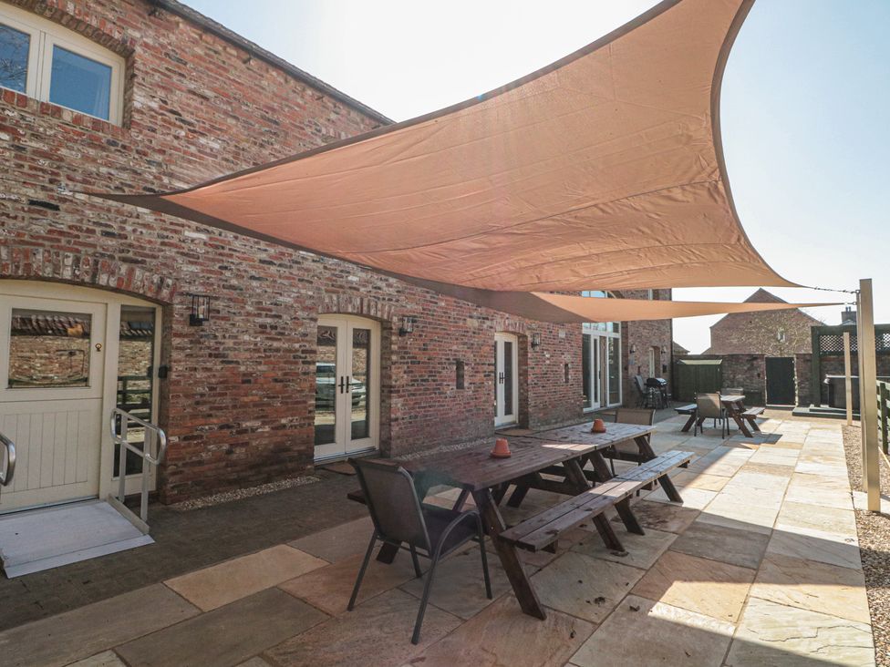An outdoor patio with picnic tables and chairs under shade sails at The Barn in Helperby near Boroughbridge