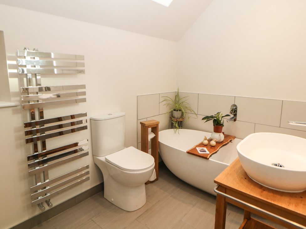 A bathroom with a toilet a freestanding bathtub with plants and a wooden tray and a sink on a wooden table at Harebell Cottage in Curbar