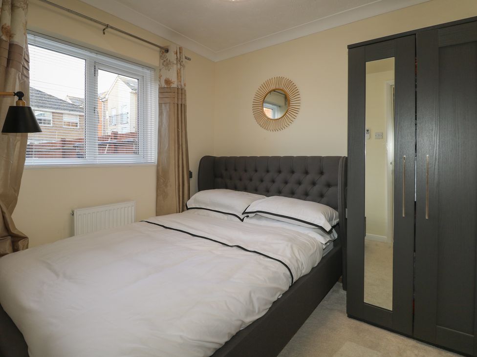 A bedroom with a double bed white bedding a black wardrobe and a window with curtains at Beach Retreat in Seaford