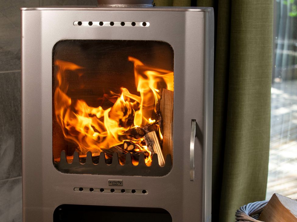 A wood burning stove with firewood burning inside next to a green curtain at Ardgartan Argyll Golden Oak in Ardgartan Loch Long