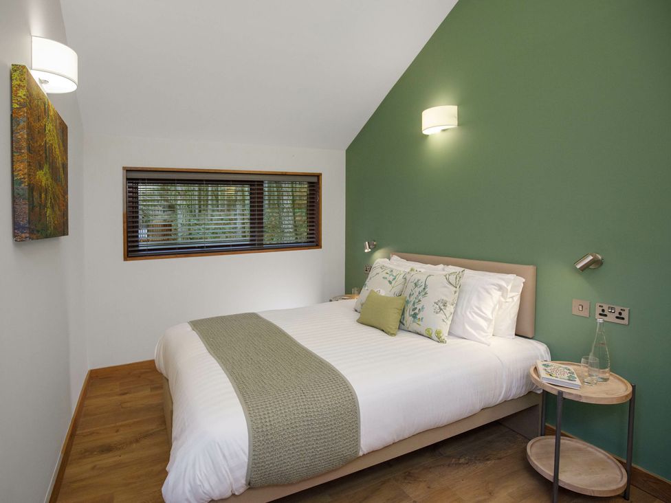 A bedroom with a double bed, green accent wall, bedside table with a glass bottle and book at Ardgartan Argyll Golden Oak in Ardgartan Loch Long